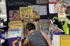 A young boy digs through a pile of books at a pop-up library at an outdoor event.
