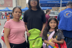 Smiling family at outdoor event holding backpacks.