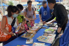 A group of men and women browsing through books on a table at an outdoor event.