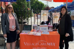 A couple of women standing next to an orange table from Village Care Max.