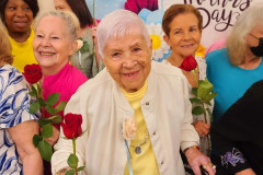 Members from an older adult center hold roses and smile during a Mother's Day celebration.