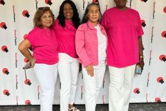 A group of women standing next to each other dressed in pink shirts and white pants.
