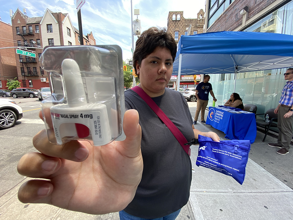 Adult holds up free NARCAN kit during an outdoor community event.